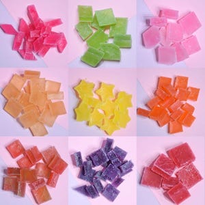 May include: A selection of colourful, translucent sweets arranged on a pink surface. The sweets are in various colours, including pink, green, orange, yellow, and purple. Some are square, others are star-shaped.