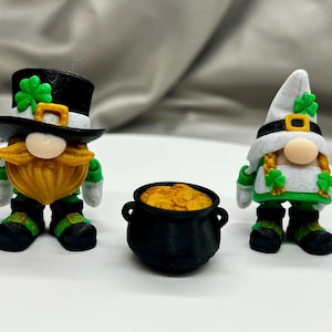 May include: Three St. Patrick's Day figurines: a leprechaun with a black top hat and a pot of gold. The leprechaun has a yellow beard, green accents, and a shamrock. A female gnome with a white hat and green accents is also present.