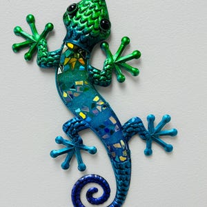 May include: A blue and green metal gecko with a curled tail. The gecko has a mosaic-like pattern and black eyes.