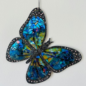 May include: A blue and green mosaic butterfly wall hanging with black glitter and pink dots around the edges.
