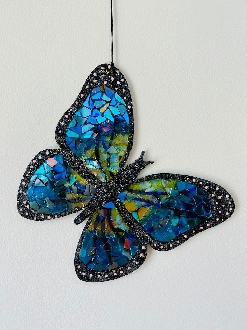 May include: A blue and green mosaic butterfly wall hanging with black glitter and pink dots around the edges.