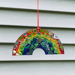 May include: A rainbow-colored glass mosaic suncatcher in the shape of an arch, hanging from a red string.