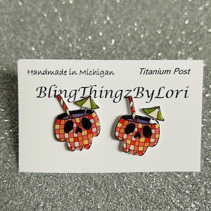 May include: A pair of skull-shaped earrings with a cocktail design. The earrings feature a plaid pattern in red, orange, and yellow, with a black skull face. Each earring has a straw and a small green and white umbrella. The text "BlingThingzByLori" is visible.