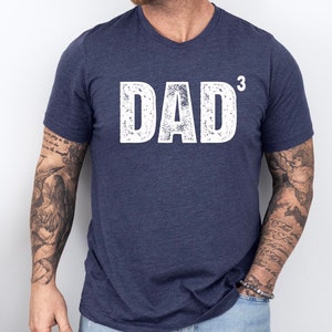 May include: A navy blue t-shirt with a white distressed graphic that says "DAD" with a superscript "3".