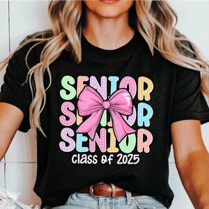 May include: A black t-shirt with a colourful graphic that says "Senior" with a pink bow in the middle and "Class of 2025" at the bottom.