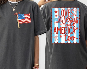 May include: Dark gray t-shirt with a small American flag graphic on the front and a larger design on the back. The back design reads "Loves Jesus and America too" in red and white, with blue accents.