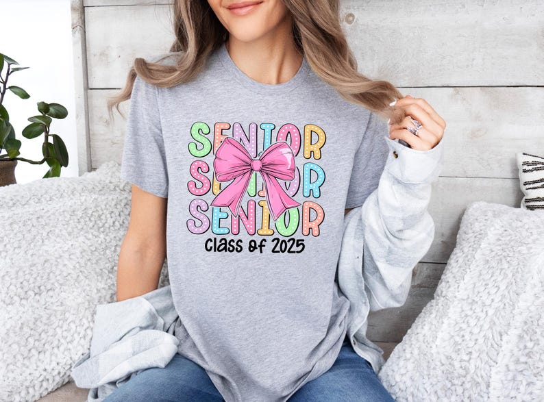 May include: A grey t-shirt with a colourful graphic design that says "Senior" with a pink bow in the middle and "Class of 2025" at the bottom.