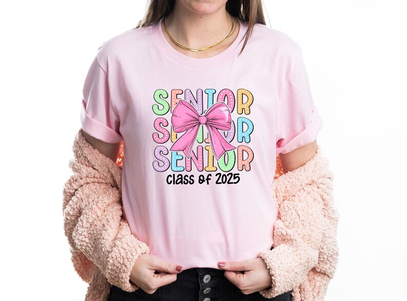 May include: Pink t-shirt with a colourful graphic that says "Senior" with a pink bow and "Class of 2025" underneath.