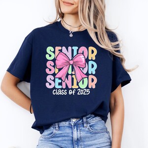 May include: Navy blue t-shirt with a colourful "Senior" graphic and a pink bow. The text "Class of 2025" is printed below the graphic.