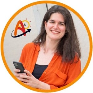 Op de afbeelding: Een vrouw in een feloranje shirt houdt een zwarte smartphone vast. Ze glimlacht en kijkt naar de camera. De achtergrond is een witte muur met een logo van een gestileerde A met een zon en een pijl.