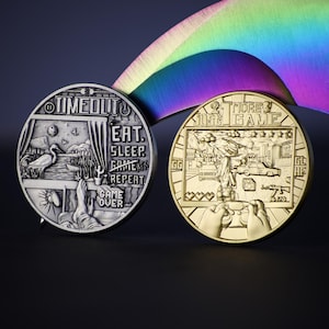 May include: Two silver and gold coins with a video game theme. The silver coin has the text "TIMED OUT" and "EAT. SLEEP. GAME. REPEAT. GAME OVER." The gold coin has the text "2 MORE JUST 1 GAME" and a pixelated video game scene.