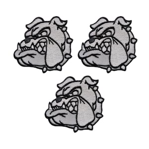 Puede incluir: Tres parches bordados con la cabeza de un bulldog con expresión enfadada. Los parches son principalmente grises con contornos negros, destacando los dientes y rasgos faciales del perro. Dispuestos en forma triangular.