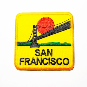 Puede incluir: Parche bordado amarillo con una silueta negra del puente Golden Gate y un sol rojo. El texto "SAN FRANCISCO" está escrito en negro debajo del puente.