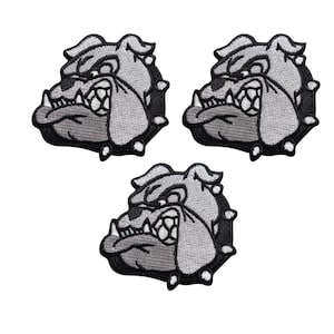 Puede incluir: Tres parches bordados con la cabeza de un bulldog en tonos grises y negros. El bulldog tiene una expresión enfadada con los dientes visibles y está rodeado por un borde negro con pequeñas púas blancas.