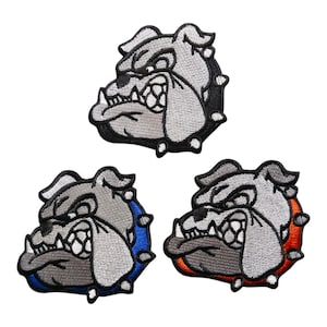 Puede incluir: Tres parches bordados con la cabeza de un bulldog en tonos grises, blancos y negros. Cada parche tiene un borde de diferente color: negro, azul y naranja. El bulldog tiene una expresión enfadada con los dientes visibles.