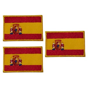 Puede incluir: Tres parches bordados con la bandera de España. Cada parche tiene forma rectangular con una franja roja en la parte superior e inferior, un centro amarillo y el escudo de armas español.