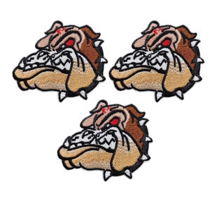 Puede incluir: Tres parches bordados con la cabeza de un bulldog. Los parches son de color beige y marrón con detalles en blanco y negro. El bulldog tiene una expresión feroz, ojos rojos y detalles puntiagudos alrededor de la cabeza.