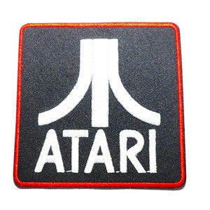 May include: A black and white embroidered patch with the Atari logo and the word "ATARI" in white text. The patch has a red border.