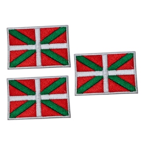 Peut inclure: Trois écussons rectangulaires avec le drapeau basque. Chaque écusson a un fond rouge, une croix blanche et des rayures diagonales vertes. Les écussons sont brodés avec une bordure blanche.