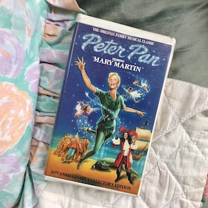 May include: A VHS tape of the musical classic "Peter Pan" starring Mary Martin. The cover features a vibrant illustration of Peter Pan, Captain Hook, and other characters against a starry night sky. The tape is a 30th Anniversary Collector's Edition.