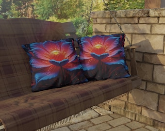 Pode incluir: Duas almofadas quadradas com um design floral vibrante em tons de vermelho, azul e amarelo. As almofadas estão colocadas sobre uma manta xadrez marrom em um balanço de madeira. O fundo apresenta uma parede de tijolos e vegetação exuberante.