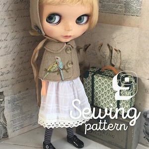 May include: A sewing pattern for a doll outfit. The pattern features a doll wearing a beige hooded jacket with embroidered birds, a white skirt with lace trim, and black and white striped tights. The doll is holding a small suitcase with a green and white floral pattern. The text "Sewing pattern" is written in a decorative font.