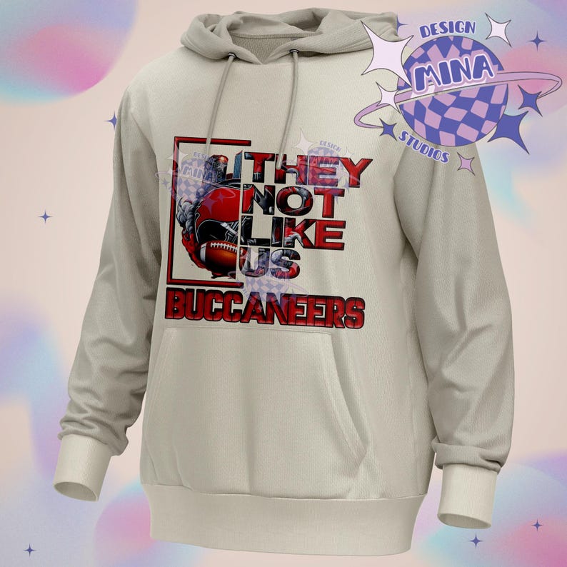 Pu&ograve; includere: Una felpa con cappuccio grigia chiaro con una stampa grafica rossa e nera di un casco da football e il testo "They Not Like Us Buccaneers".