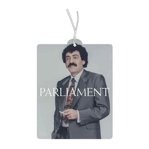 May include: A vintage style air freshener with a photo of a man with a mustache wearing a suit and tie. The air freshener has the word "PARLIAMENT" printed on it.