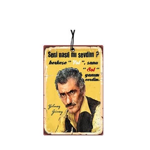 Pode incluir: Um pôster de estilo vintage com um retrato de Yilmaz Güney, um ator e diretor turco. O pôster tem um fundo amarelo com detalhes vermelhos e brancos. O texto no pôster diz "Seni nasil mi sevdim? herkese "Yol", sana "Sol" yanım verdim."