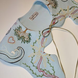 May include: A light blue embroidered collar with a whimsical design. The collar features embroidered trees, suns, hearts, and waves in shades of green, yellow, red, and black. The brand name "STARUSHKO" is visible on a tag.