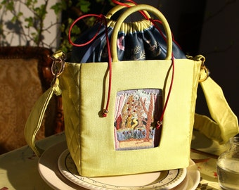 Puede incluir: Bolso de mano amarillo claro con diseño acolchado y parche bordado rectangular con escena de bosque. El bolso tiene cierre de cordón con estampado floral y cordones rojos. Incluye correa para el hombro y asas superiores.