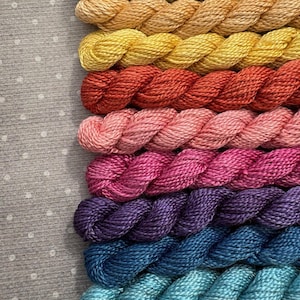 May include: A collection of colorful embroidery floss in a gradient of colors. The floss ranges from olive green to light blue, with shades of yellow, orange, red, pink, and purple in between. The threads are neatly arranged, showcasing their vibrant hues.