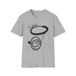 Peut inclure: T-shirt gris clair avec un dessin de tuba noir et le mot "Tuba!" au-dessus. L'illustration du tuba comprend un embout buccal, des pistons et un pavillon, le tout dans un style simple et ludique.