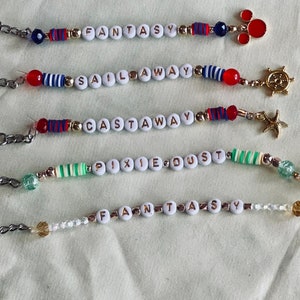 May include: Five keychains with different colored beads and charms. The keychains spell out the words "Fantasy", "Sail Away", "Castaway", "Pixie Dust", and "Fantasy".