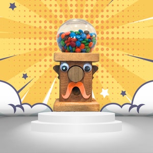 May include: A wooden gumball machine with a cartoon face, featuring a brown nose, blue eyes, and a red mustache. The machine is filled with colorful gumballs and is set against a yellow and white polka dot background.