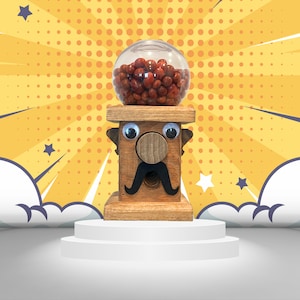 May include: A wooden candy dispenser shaped like a face with googly eyes, a brown mustache, and a red nose. The dispenser has a clear plastic candy jar on top filled with red and brown candies.