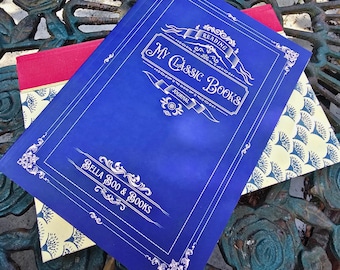May include: A blue reading journal titled My Classic Books by Bella Boo & Books with white decorative borders and text. Beneath it lies a second book featuring a red spine and a cream-colored cover with a repeating blue fan-shaped pattern.
