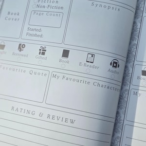 May include: Close-up of a book journal page with sections for recording book details. Features include fields for 'Fiction' or 'Non-Fiction', 'Page Count', 'Synopsis', and 'Rating & Review'. Includes icons for 'Book', 'E-Reader', and 'Audio'.