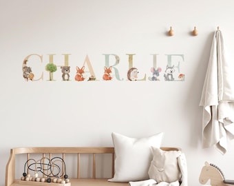 May include: A white wall with the name "CHARLIE" spelled out in large letters. Each letter is decorated with a different woodland animal, including a fox, a bear, a hedgehog, and a squirrel. The letters are on a light blue background with a white border.