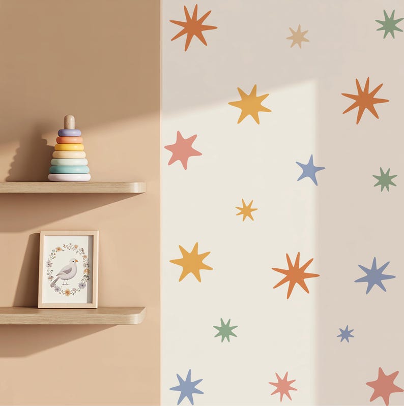Op de afbeelding: Een muursticker set met veelkleurige stervormen in tinten oranje, geel, blauw, groen en roze. De sterren zijn in een verspreid patroon op een lichte muur geplaatst. Twee houten planken bevatten een stapelspeelgoed en een ingelijste vogelprint.
