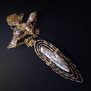May include: A gold-coloured necklace featuring a large, iridescent, oblong pearl pendant. The pendant is framed by layered, wavy gold wire. The necklace also has smaller, round pearls set in gold wire designs, connected by a delicate chain.