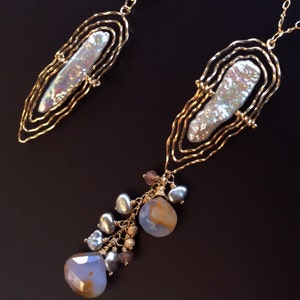 May include: Two gold necklaces with irregular shapes. Each has a large, iridescent pearl set in a wireframe. One necklace features a cluster of blue and brown gemstones and pearls.