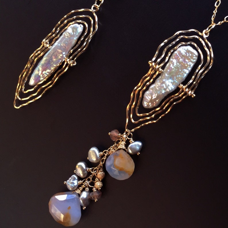 May include: Two gold necklaces with irregular shapes. Each has a large, iridescent pearl set in a wireframe. One necklace features a cluster of blue and brown gemstones and pearls.