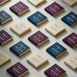 May include: Arrangement of personalized chocolate bars with gold foil edges. Each bar features the names "AMELIA ARTHUR" and a date within a decorative frame. The bars are in various colors, including cream, navy, and burgundy.