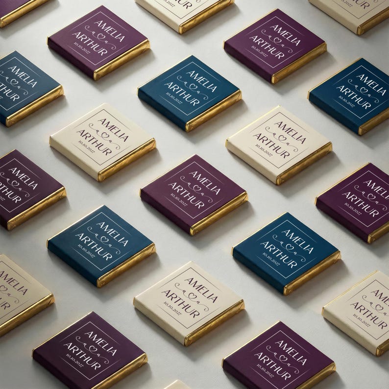 May include: Arrangement of personalized chocolate bars with gold foil edges. Each bar features the names "AMELIA ARTHUR" and a date within a decorative frame. The bars are in various colors, including cream, navy, and burgundy.