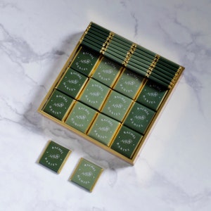 Op de afbeelding: Een doos met groene en gouden chocoladegeschenken met de namen "Rachel" en "Daniel" gedrukt op elk stuk.