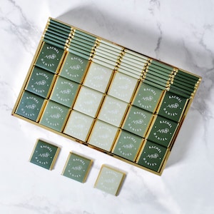 Op de afbeelding: Een doos met groene en gouden chocolade-favorieten met de namen "Rachel" en "Daniel" gedrukt op elk stuk.