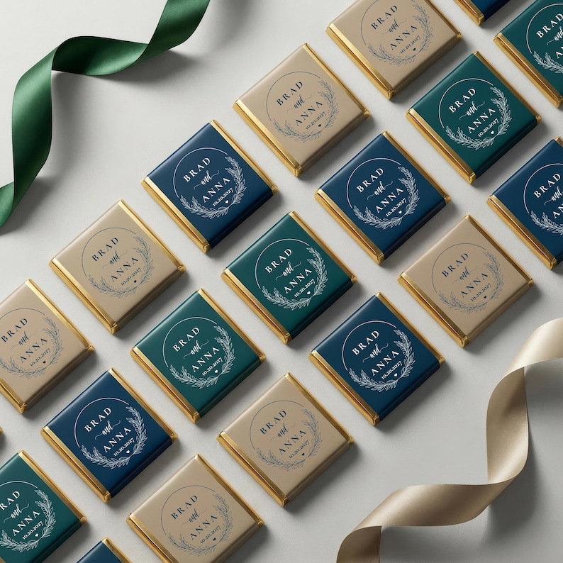 May include: Arrangement of personalized chocolate squares with gold foil edges. Each square features the names "Brad and Anna" and a date within a circular wreath design. The squares are in shades of blue, green, and tan, with ribbons in matching colors.
