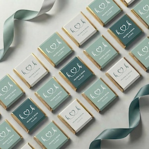 May include: Arrangement of personalized chocolate bars with gold edges. Each bar features a heart design with the initials "h" and "k", along with the names "Helena & Kevin" and the date "11.11.2027". The bars are in shades of green and white.