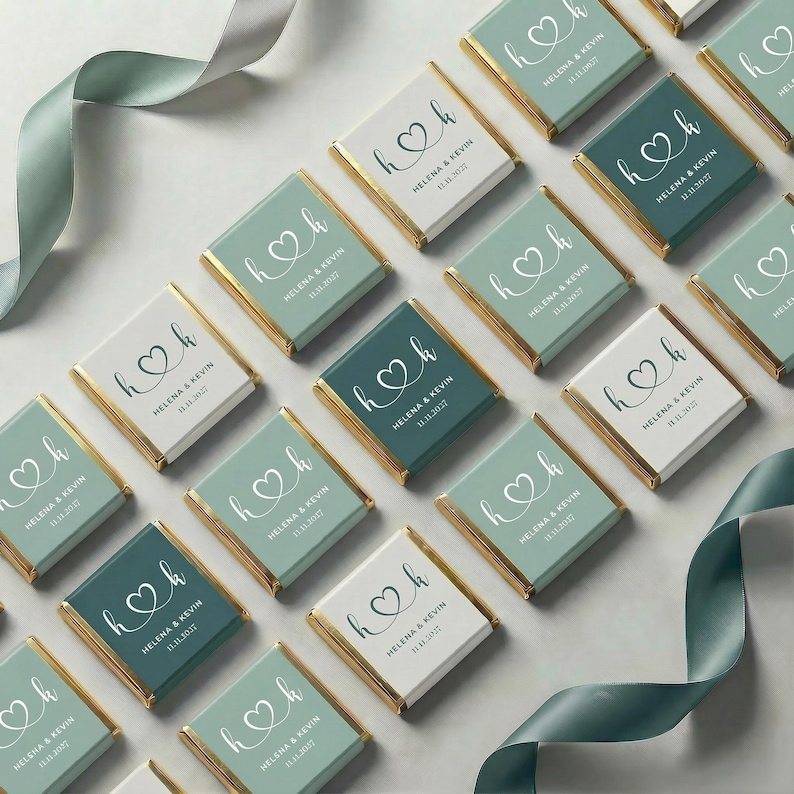 May include: Arrangement of personalized chocolate bars with gold edges. Each bar features a heart design with the initials "h" and "k", along with the names "Helena & Kevin" and the date "11.11.2027". The bars are in shades of green and white.